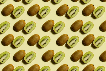 Kiwi pattern. Repetition of kiwi halves on a light yellow background. Top view of green and brown kiwi halves on a light surface. Horizontal. The concept of healthy food and vegetarianism.