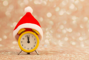 yellow alarm clock with red santa hat, time from five to 12, five minutes to new year