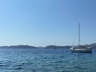 Sailing on blue turquoise waters of Aegean Sea. White yacht in the bay and islands at the horizon. Clear blue skies. 