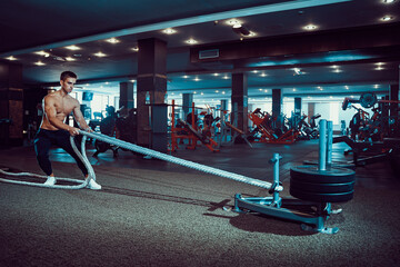 Fitness man working out with battle ropes at gym.