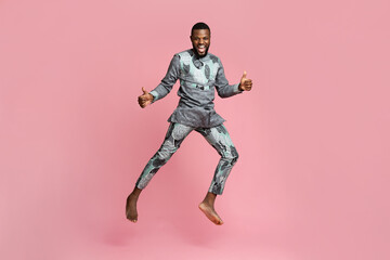 Fototapeta na wymiar Joyful black guy showing thumbs up and jumping on pink