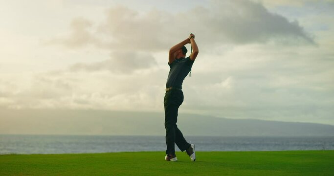 Sunset golf, man swinging and hitting golf ball at sunset on beautiful golf course by the ocean, slow motion