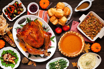 Classic Thanksgiving turkey dinner. Above view table scene on a dark wood background. Turkey, mashed potatoes, dressing, pumpkin pie and sides.
