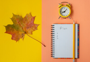 Open checkered notebook, yellow autumn maple leaf, top view. Autumn flat lay. Fall plan, layout
