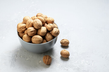 Untreated walnut in a bowl on a grey concrete background with a copy-space.