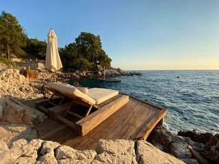 Sunbed and sun shade on a wooden sun deck on the rocks, next to wavy sea. Romantic holiday and...