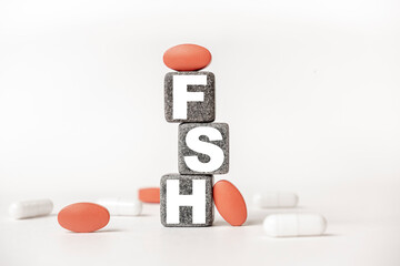 a group of white and red pills and cubes with the word FSH Follicle stimulating hormone on them, white background. Concept carehealth, treatment, therapy.