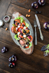 Fototapeta na wymiar Healthy salad with vegetables, nuts and cheese in a vintage plate on a wooden table. Black tomato salad. Flat lay.