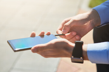 Cropped shot of a businessman using flash drive for smartphone while working outdoors on a sunny day, focus on male hands