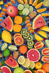 Fototapeta na wymiar Tropical & citrus fruit for good health forming an abstract background. High in antioxidants, fibre, anthocyanins, lycopene, vitamins & minerals. Immune boosting food. Flat lay on mottled blue.