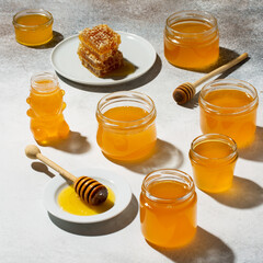 Jars of honey  and sweet honeycomb on light table. Many glass cans of various shapes.