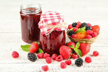 Sweet jam in glass jars with ripe berries on white wooden table