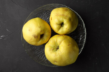 three quinces on a glass plate, dark concrete background, top view.