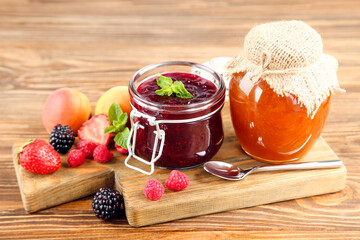 Sweet jam in glass jars with ripe berries on brown wooden table