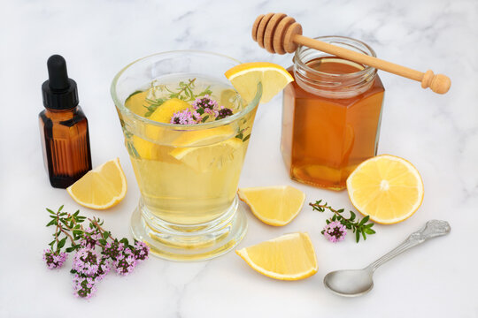 Alternative Medicinal Remedy For Cold & Flu Virus With Thyme Herb, Honey & Lemon In Glass With Essential Oil. Immune Boosting Medication, Is Anti Bacterial, Antiseptic And Anti Viral. On Marble.