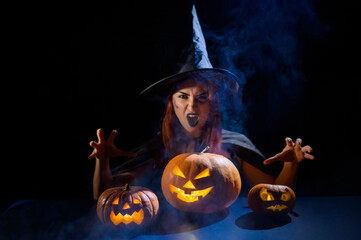 The evil witch casts a spell on pumpkins. Portrait of a woman in a carnival halloween costume in...