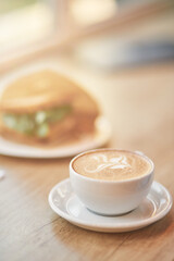 Vertical close up shot of of a cup of coffee cappuccino and sandwich on wooden table in cafe, selective focus