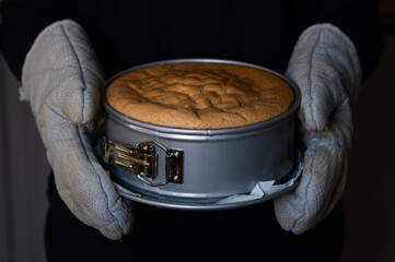 a freshly baked hot cake in a springform pan is held with gloves