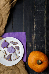Pumpkin and Halloween cookies on white plate, sackcloth on black wooden background. Hallooween trick or treat concept. Copy space. Vertical shot.