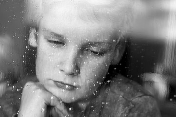 the head of the boy's face is sad sad photo through glass with drops of black-and-white photo of a depression stress