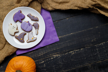Pumpkin and Halloween cookies on white plate, sackcloth on black wooden background. Hallooween trick or treat concept. Copy space.