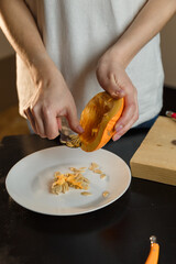 Woman taking out the seeds from  pumpkin on kitchen board, only hands visible. Autumn seasonal vegetables cooking. Healthy eating habits, organic vegetarian food concept.