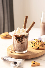 Milkshake with ice cream, marshmallows and chocolate, a glass with a milkshake on a wooden board, chocolate chip cookies and a bottle of cocoa