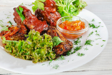Grilled fried meat on a plate with salad and herbs, shish kebab in tomato sauce