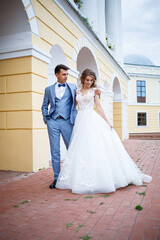 Young stylish guy in the costume of the groom and the bride beautiful girl in a white dress with a train walk in the park on their wedding day