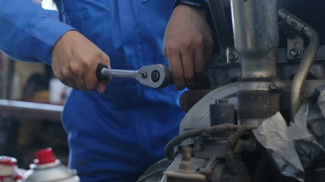 Mechanic Asian man close up fixing repairing car engine automobile vehicle parts examining using tools wrench equipment working hard in workshop garage support and service in overall work uniform