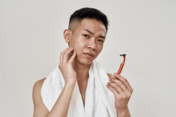 Portrait of young asian man with problematic skin holding a razor, looking at camera with...