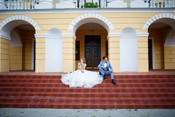 Young stylish guy in the costume of the groom and the bride beautiful girl in a white dress with a train walk in the park on their wedding day