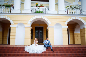 Fototapeta premium Young stylish guy in the costume of the groom and the bride beautiful girl in a white dress with a train walk in the park on their wedding day