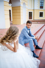Fototapeta premium Young stylish guy in the costume of the groom and the bride beautiful girl in a white dress with a train walk in the park on their wedding day