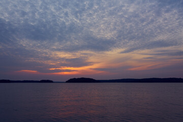 Colorful cloudy sky on a sunset over the sea with horizon on a background and reflection on water.