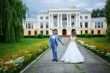 Obraz premium Young stylish guy in the costume of the groom and the bride beautiful girl in a white dress with a train walk in the park on their wedding day