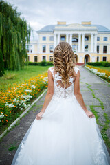 beautiful girl bride in a white dress with a train and a walk turned against the background of a large house with columns on their wedding day