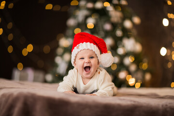 Young baby boy in Christmas cap laying on a bed against Christmas background.