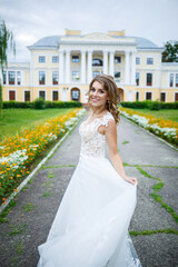 Fototapeta premium beautiful girl bride in a white dress with a train and a walk turned against the background of a large house with columns on their wedding day