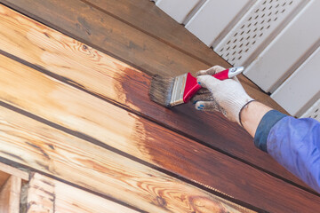 Daylight. a person with the help of a brush applies to the facade of a wooden house, a special...