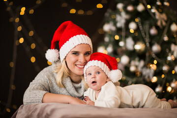 Fototapeta na wymiar Woman and young baby boy in Christmas cap laying on a bed against Christmas back