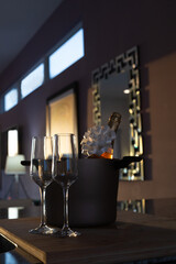 Wine glasses and bottle ice bucket in dark room at sunset lit by natural sunlight from a window waiting for people to drink and enjoy it