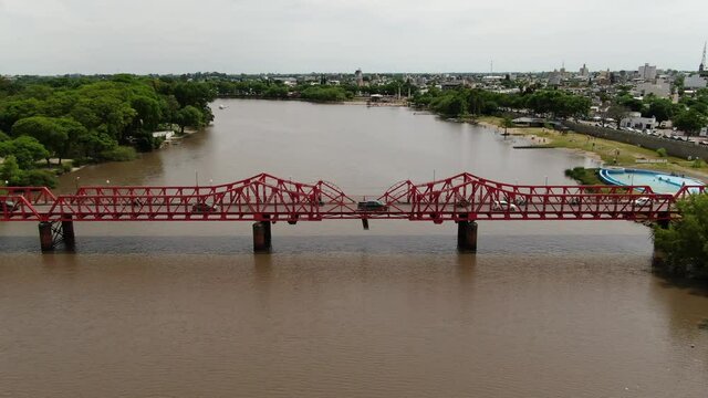 Video a&eacute;reo del r&iacute;o y las m&aacute;rgenes del r&iacute;o que circula por la ciudad y un puente rojo construido de metal remachado.