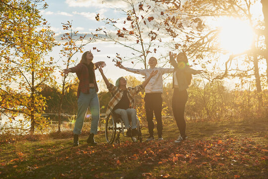 Disabled teen boy playing in Fall leaves with a multi ethnic group of friends.