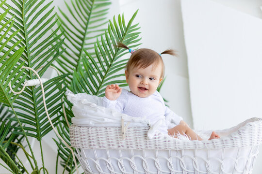 happy little baby girl sitting in a beautiful stroller in a white bodysuit at home