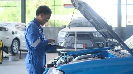 Mechanic Asian man using laptop computer examining tuning fixing repairing car engine automobile vehicle parts using tools equipment in workshop garage support and service in overall work uniform