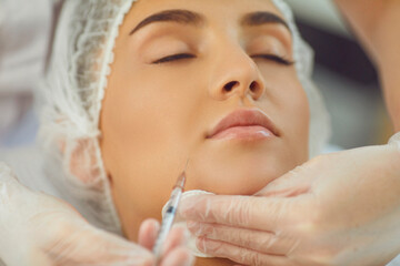 therapists hands in gloves with syringe and cotton pad making botox filler injection in womans underlip