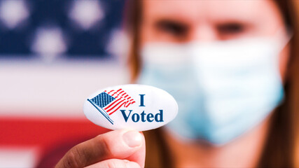Woman with face mask showing I voted sticker with american flag. Extreme close-up