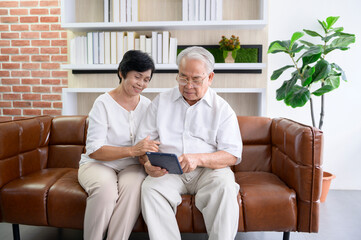 Obraz premium A happy senior Asian couple is using tablet and talking with family on webcam at home, retirement concept.