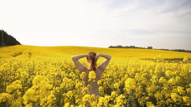 Cute naturist woman enjoys Spring in rapeseed field without clothes